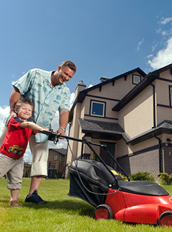 Father and son mowing yard in front of home